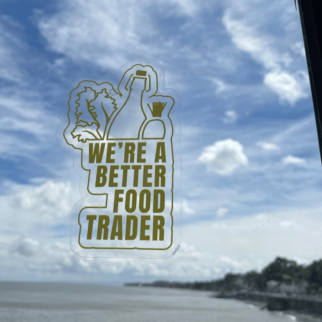 The image is of a window sticker that says 'We're a Better Food Trader' on a window with the sea behind it
