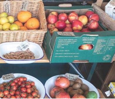 Farm shop shelves showing apples, oranges and tomatoes